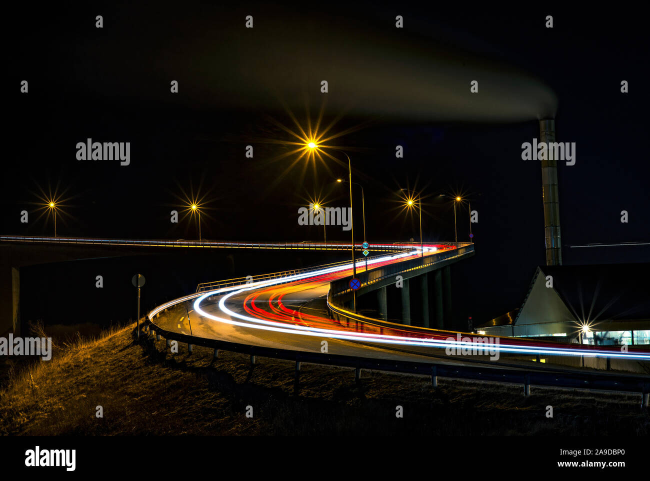 Automobili che guidano su un ponte di notte lasciando i sentieri del semaforo. Foto Stock