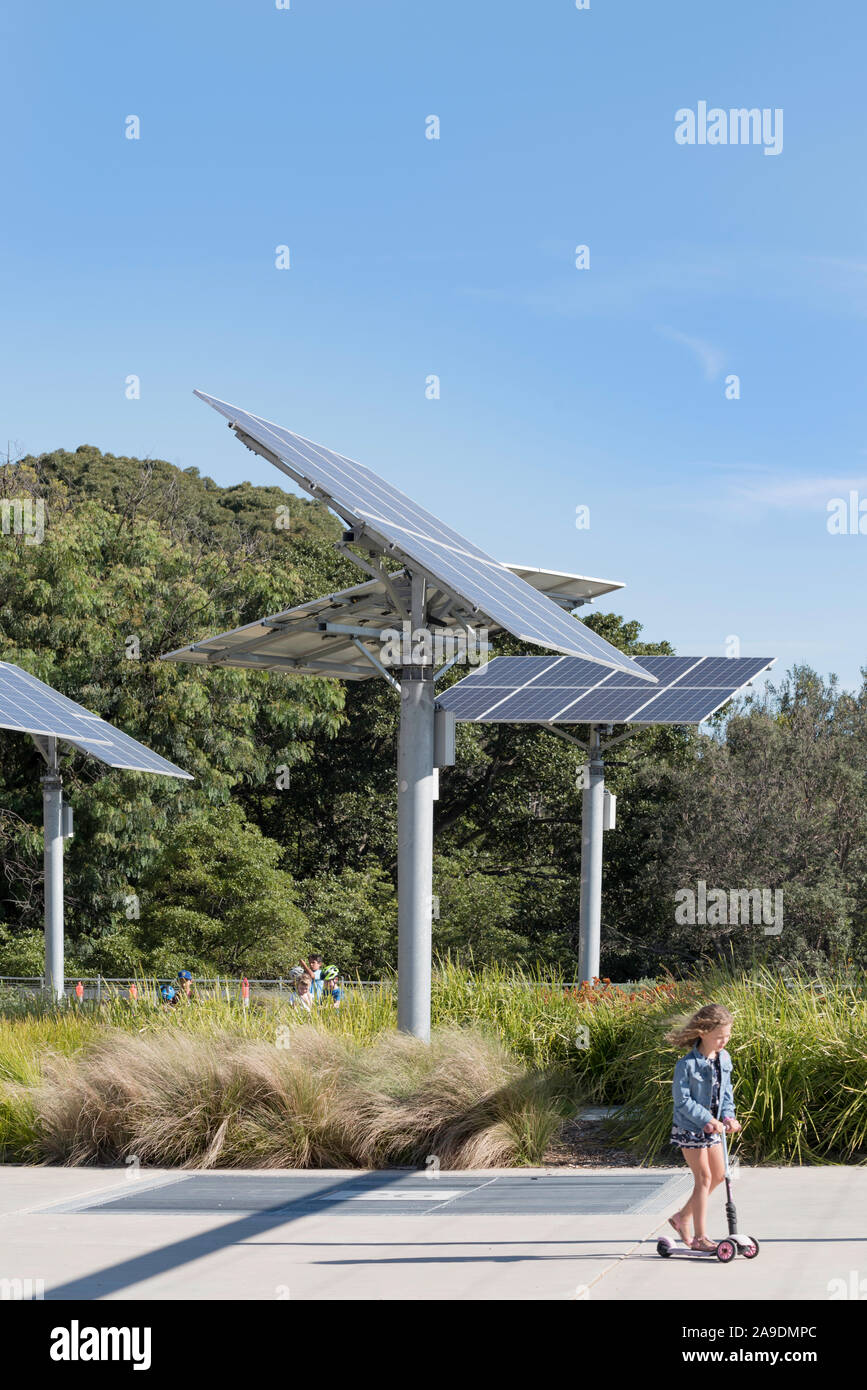 I bambini giocano e ride scooter vicino polo regolabile montato su pannelli solari in un giardino e un parco pubblico a sfere riserva di testa a Sydney in Australia Foto Stock
