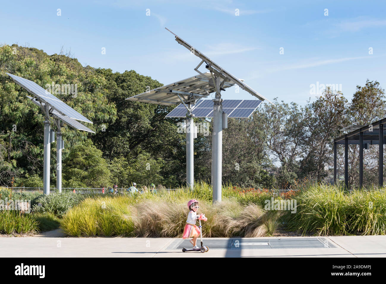 I bambini giocano e ride scooter vicino polo regolabile montato su pannelli solari in un giardino e un parco pubblico a sfere riserva di testa a Sydney in Australia Foto Stock