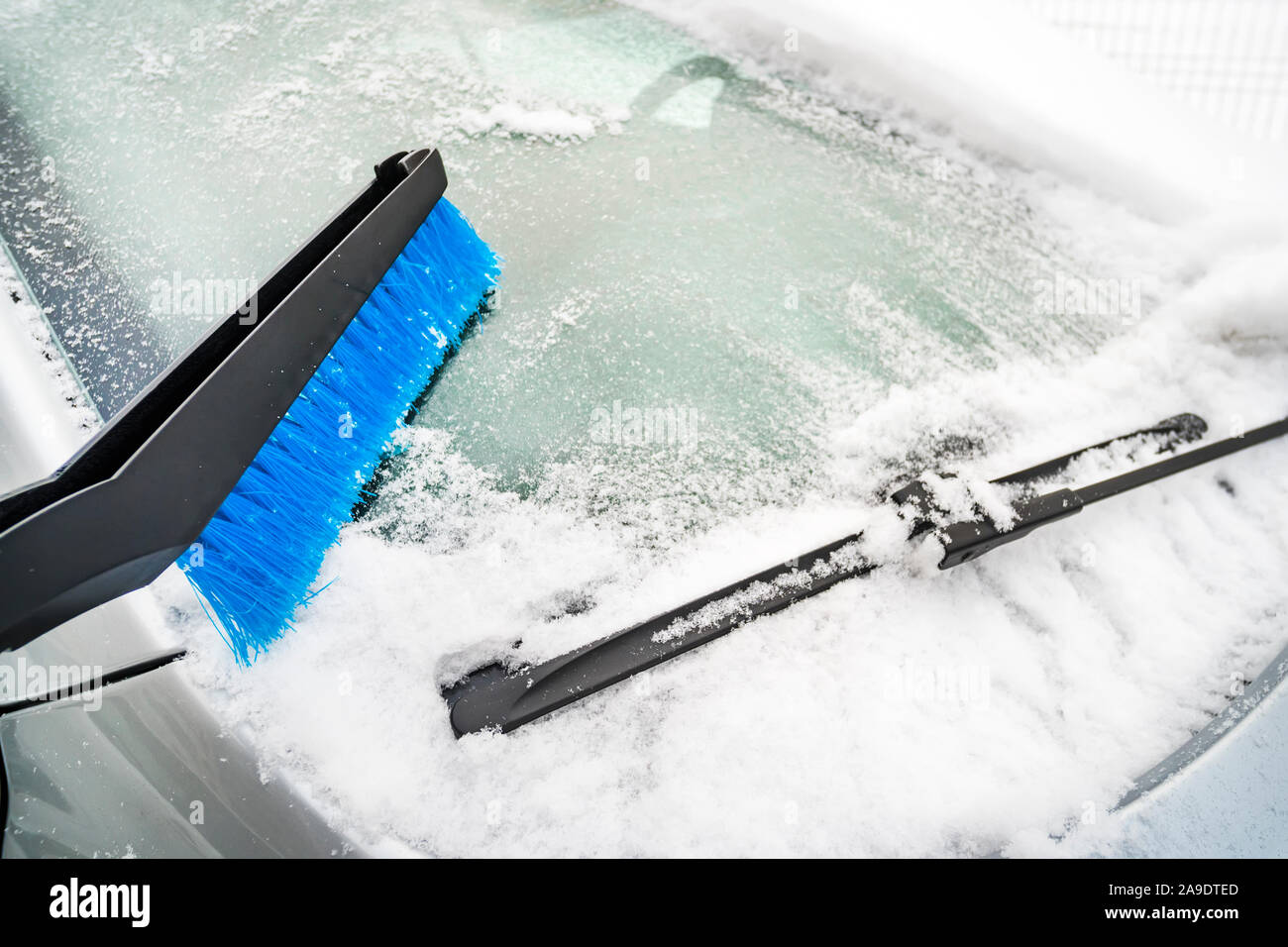 Blue spazzola in plastica pulizia di neve. Spalare la neve da automobile con dettagli cromati. Grigio al di fuori auto coperti di neve e ghiaccio. Congelati vetro del finestrino Foto Stock