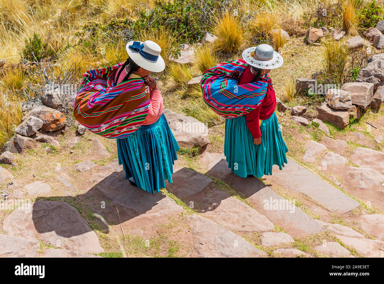 Due Quechua donne indigene in abiti tradizionali e prodotti tessili camminando giù i passaggi sulla isola di Taquile dal Lago Titicaca Puno, Perù. Foto Stock