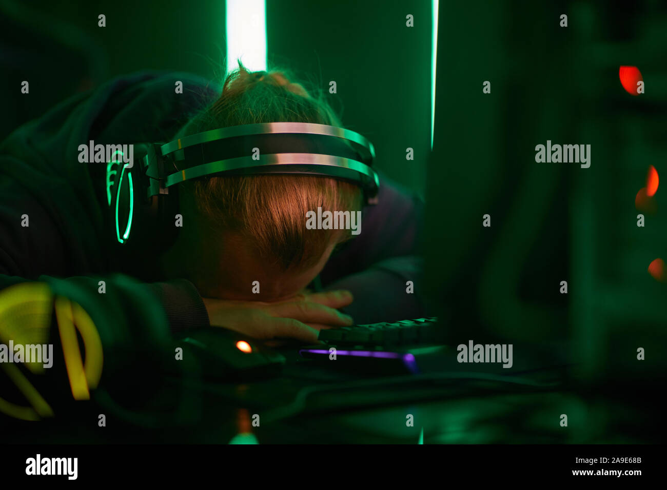 Giovane programmatore di computer nelle cuffie sdraiato su un tavolo e dormire egli stanco dopo il lavoro Foto Stock