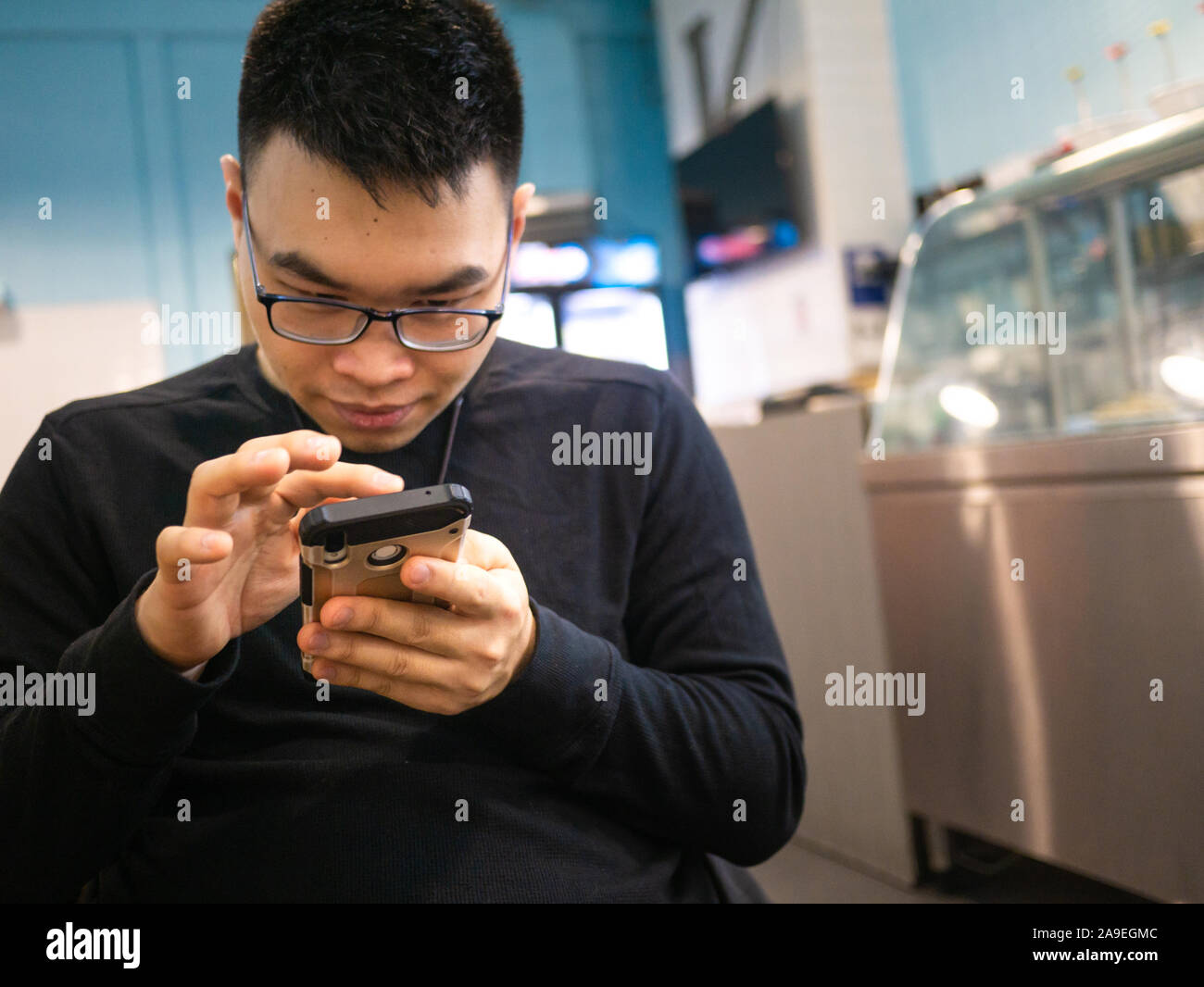 Uomini asiatici concentrandosi su smartphone nel ristorante pubblico. La digitazione di messaggio sul cellulare Foto Stock