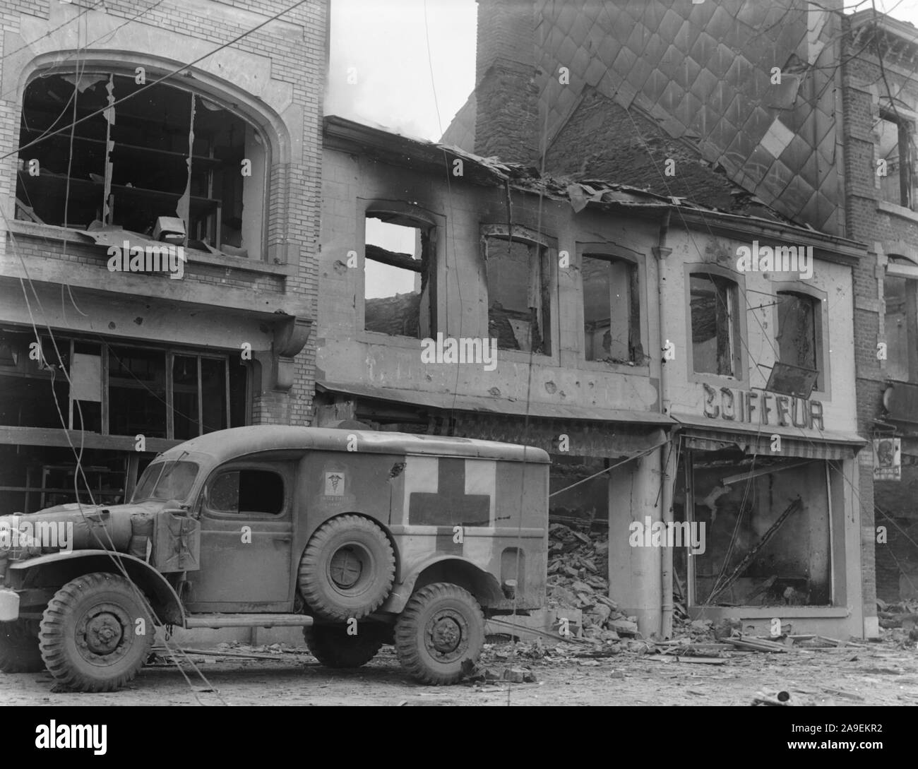 American ambulance attende al di fuori di un edificio bombardato a Bastogne, Belgio, mentre un ricercatore cerca persone ferite durante i dieci giorni di difesa dal 101st Airbrne Div dicembre26, 1944 Foto Stock