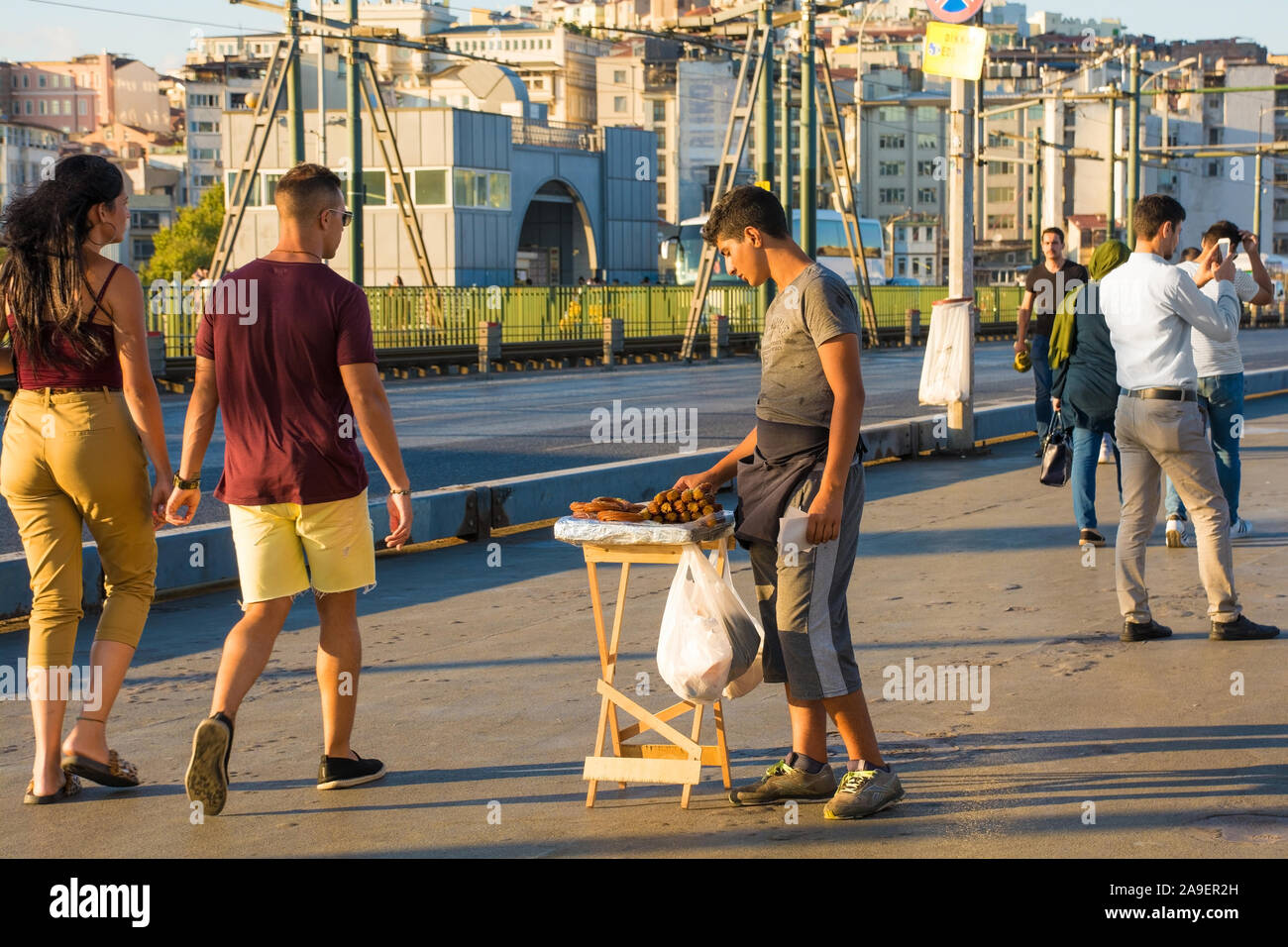 Istanbul,Turkey-September 6 2019. Un giovane produttore alimentare vende dolci fritti dolci per i passanti sul Ponte di Galata nel tardo pomeriggio di sole estivo Foto Stock