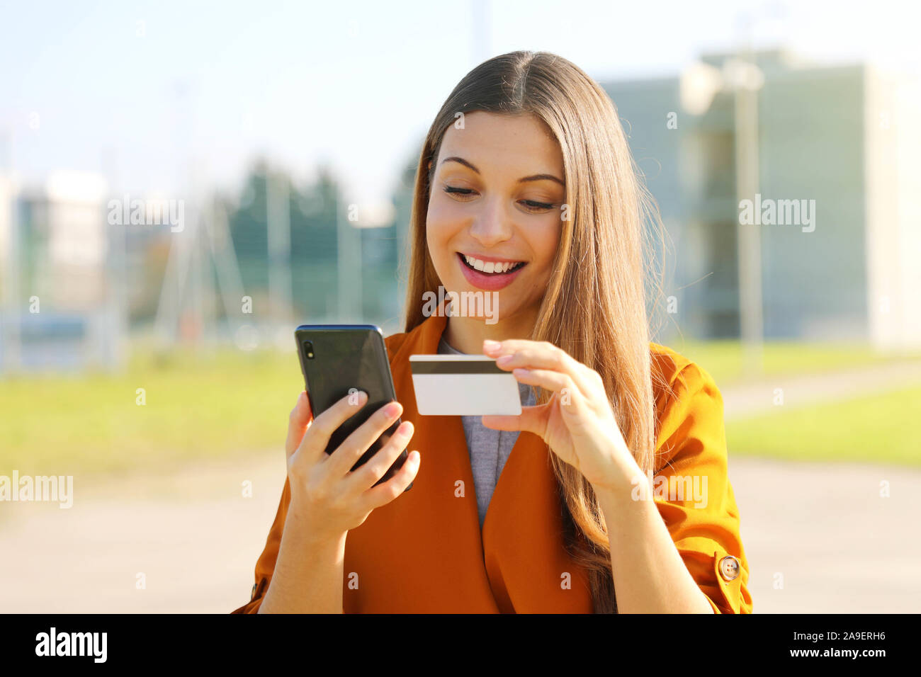 Close up di Pretty Woman leggere il numero di carta di credito facendo il pagamento on-line con il suo telefono cellulare al di fuori. Foto Stock