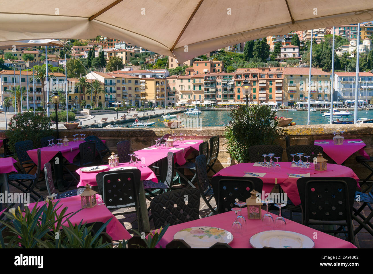 Porto Santo Stefano, Italia - 22 Settembre 2013: ristorante all'aperto con tavolo luminoso impostazioni e vista sul lungomare della baia con barche e palme Foto Stock