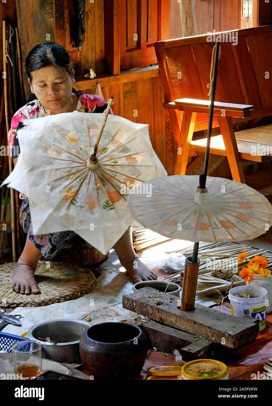 Giovane e graziosa donna birmana che dipinge sapientemente carta parasol fatta a mano circondata da pitture e pennelli. In palafitte casa sul lago Inle, Myanmar Foto Stock Giovane e graziosa donna birmana che dipinge sapientemente carta parasol fatta a mano circondata da pitture e pennelli. In palafitte casa sul lago Inle, Myanmar Foto Stock
