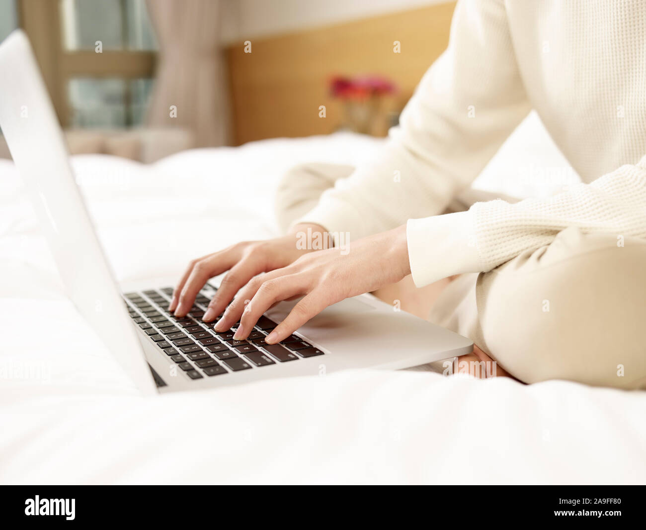 Giovane donna asiatica seduta sul letto a lavorare utilizzando il computer portatile, concentrarsi sulle mani Foto Stock