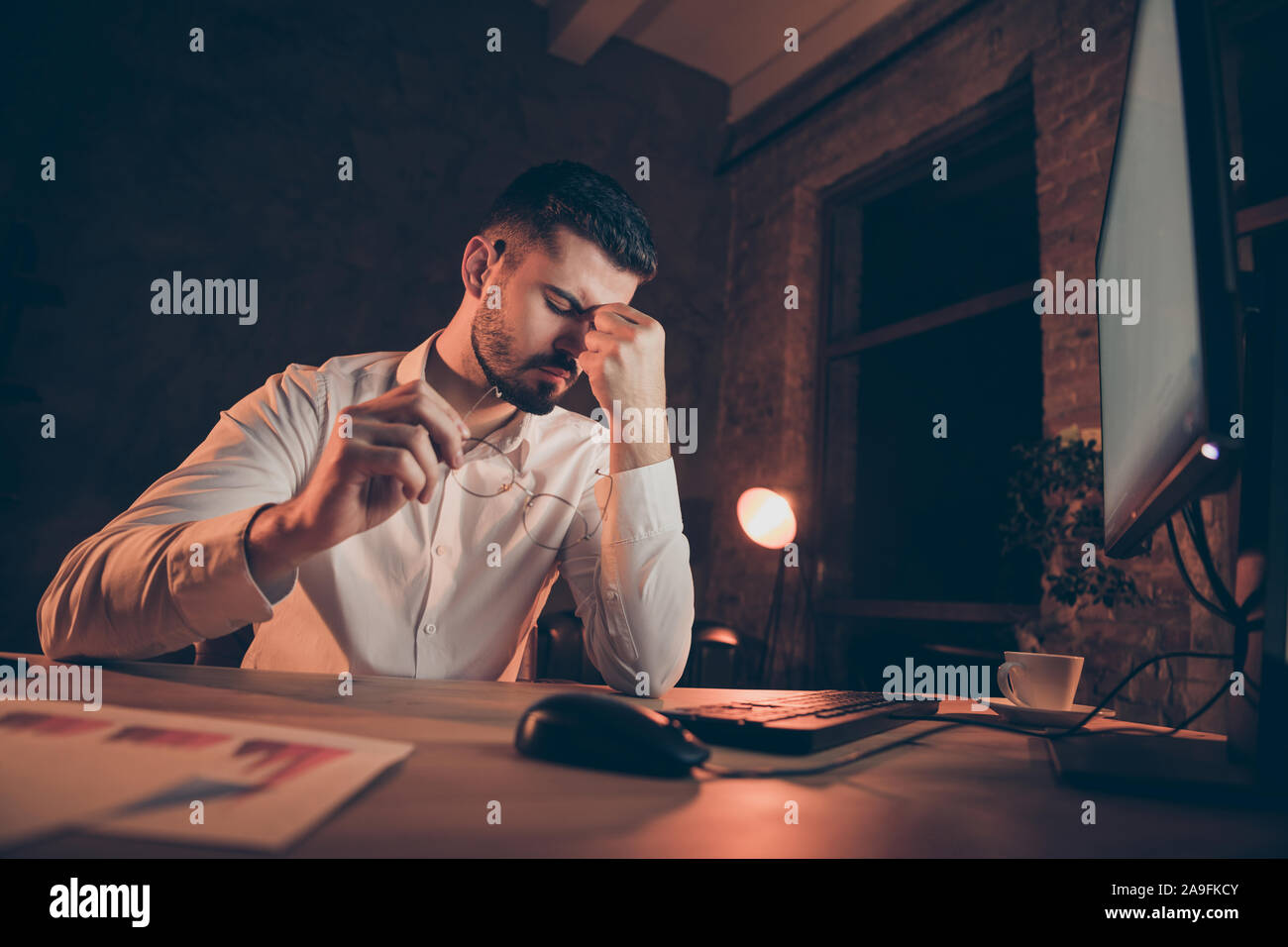 Basso angolo di seguito visualizzare foto di stanchi imprenditore con testa emicrania male gli occhi dolorante di mettere gli occhiali off seduto alla scrivania Foto Stock