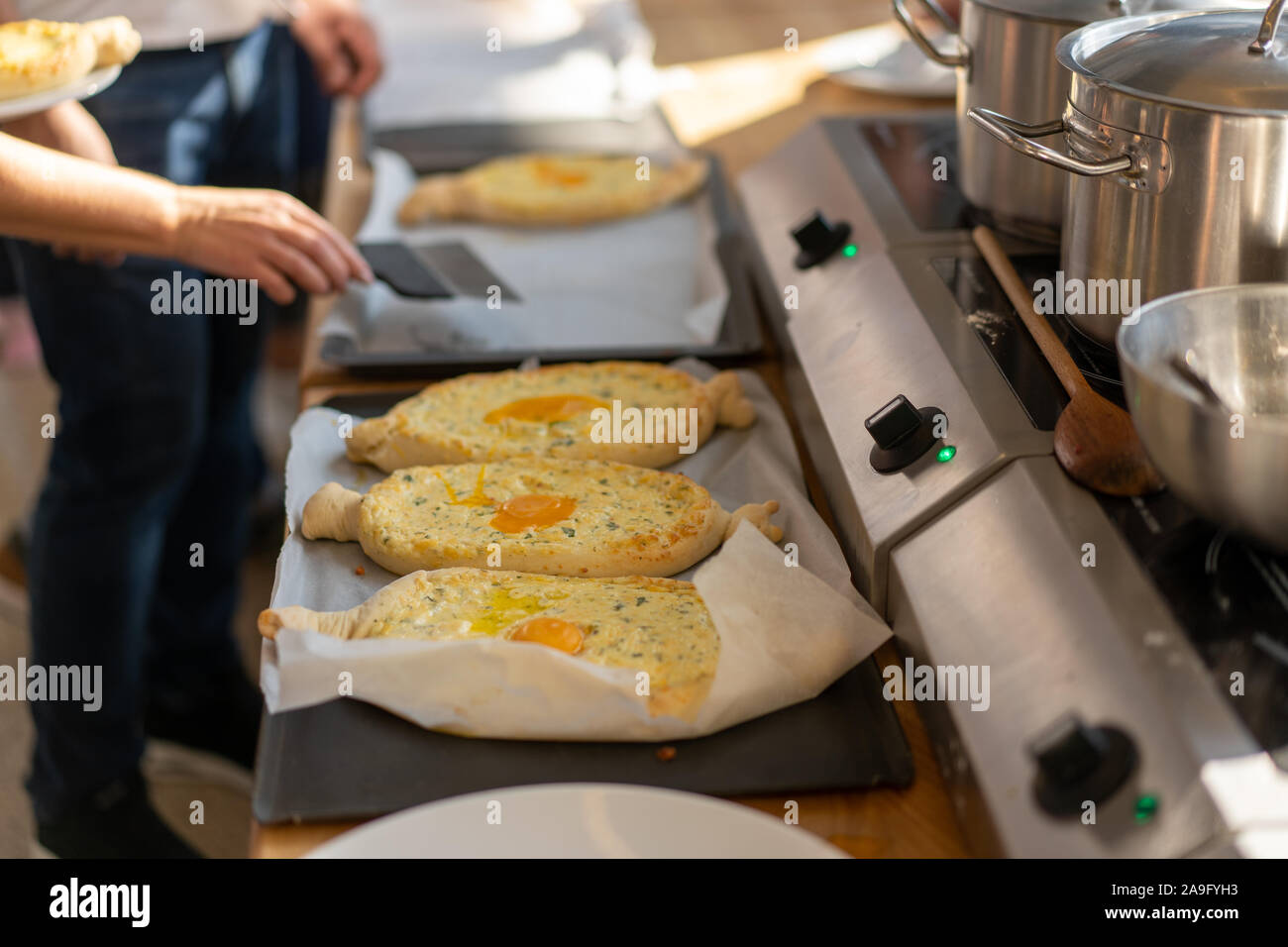 Delizie master class. Primo piano delle mani di persone preparando khachapuri. In stile georgiano tradizionale pane di formaggio. Il cibo in stile georgiano. Grande famiglia irriconoscibile cooki Foto Stock