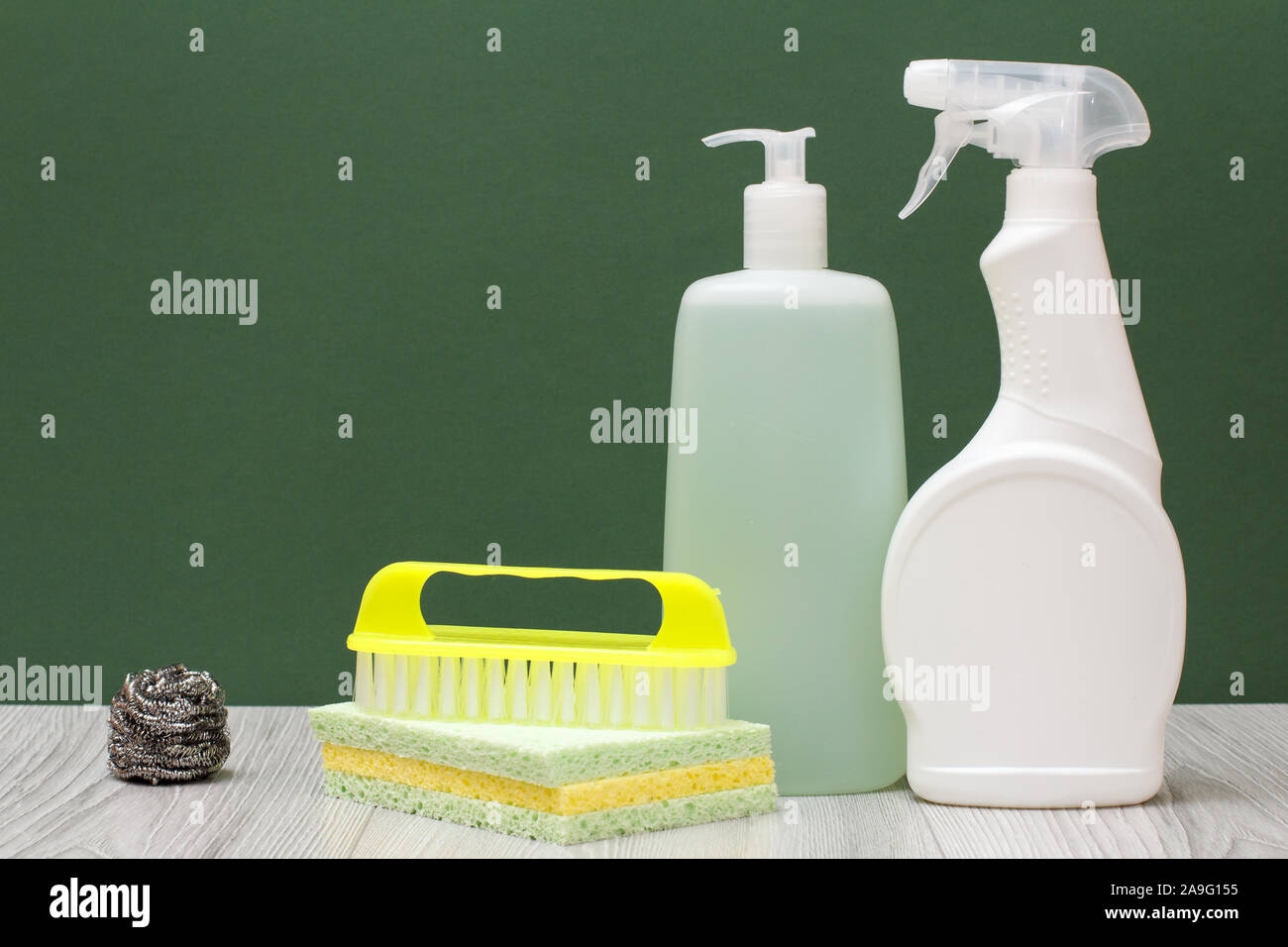 Le bottiglie di plastica di detergente per forni a microonde e fornelli, vetro e tile cleaner spazzola e spugne su pavimenti in laminato e sfondo verde. Lavare Foto Stock