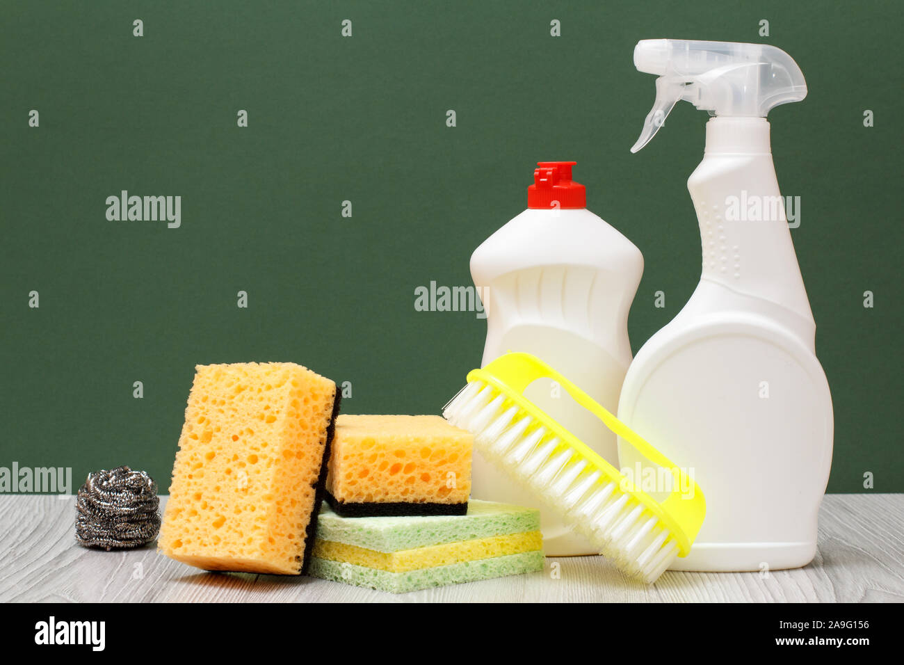 Le bottiglie di plastica di detersivo liquido per stoviglie, vetro e tile cleaner spazzola e spugne su pavimenti in laminato e sfondo verde. Lavaggio e pulizia conce Foto Stock