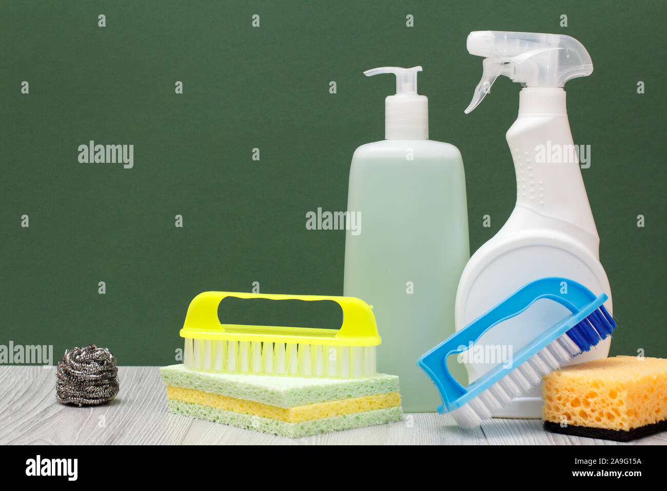 Le bottiglie di plastica di detergente per forni a microonde e fornelli, vetro e tile cleaner, spazzole e spugne su pavimenti in laminato e sfondo verde. Wa Foto Stock