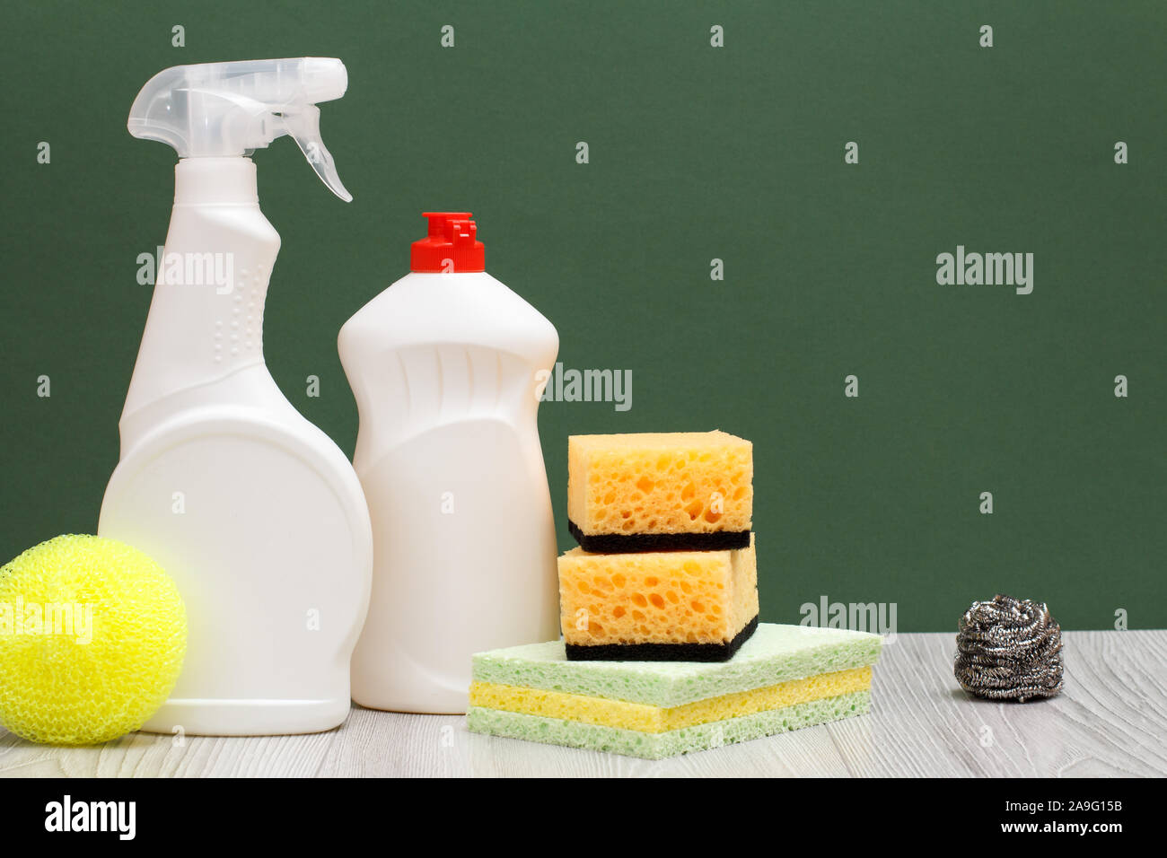 Le bottiglie di plastica di detersivo liquido per stoviglie, vetro e detergente per piastrelle e spugne su pavimenti in laminato e sfondo verde. Il lavaggio e la pulizia di concetto. Foto Stock