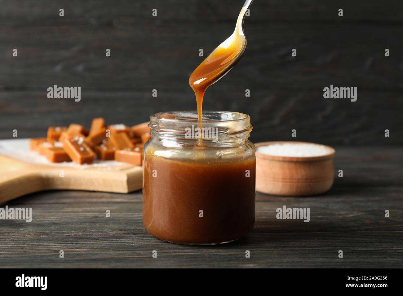 Vaso di vetro con caramello salato e caramelle su sfondo di legno, lo spazio per il testo Foto Stock