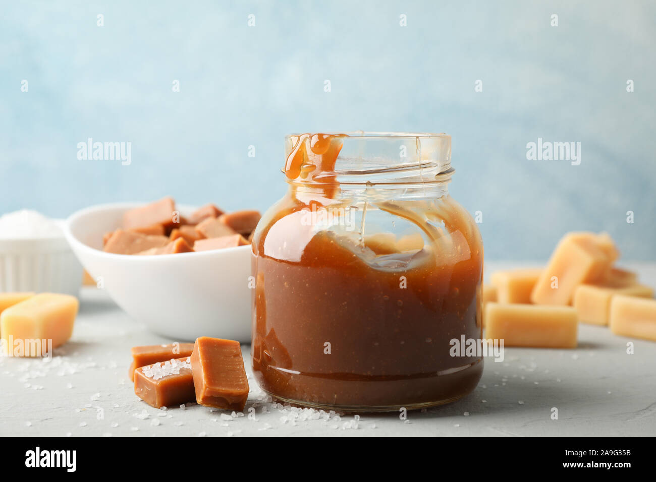 Vaso di vetro con caramello salato e caramelle su sfondo grigio, spazio per il testo Foto Stock