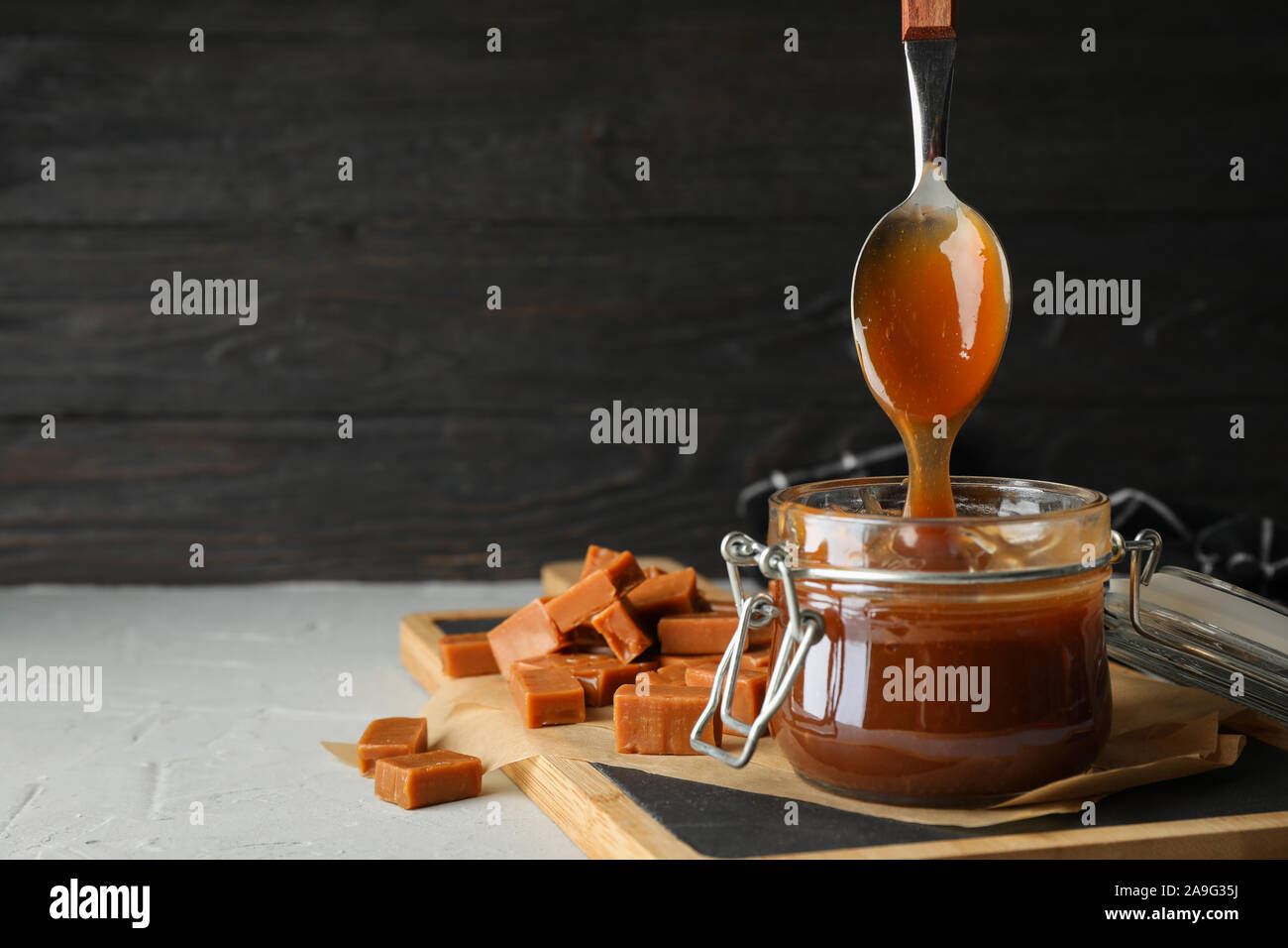 Vaso di vetro con caramello salato e caramelle su sfondo grigio, spazio per il testo Foto Stock