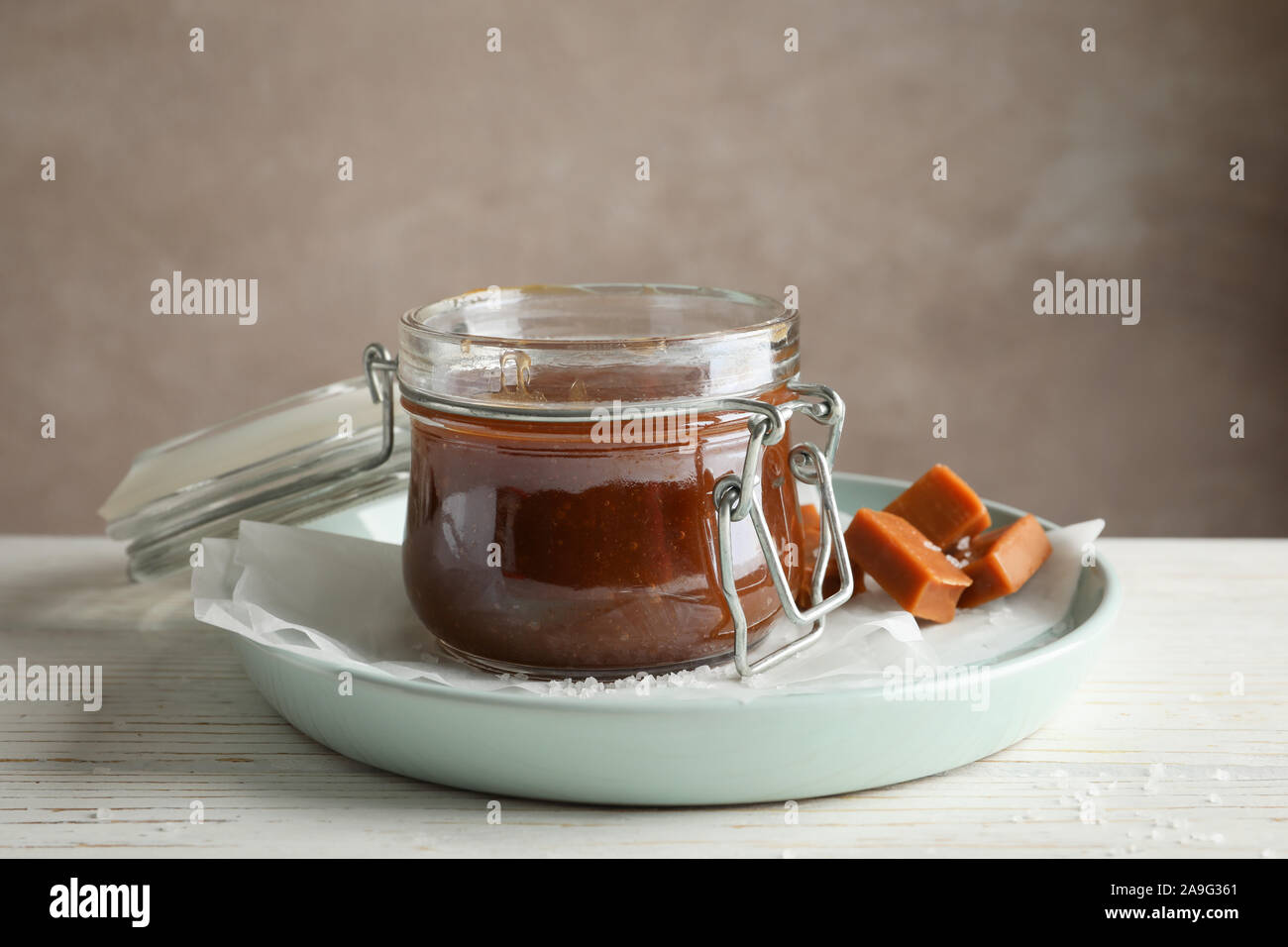 Vaso di vetro con caramello salato e caramelle su sfondo di legno, lo spazio per il testo Foto Stock