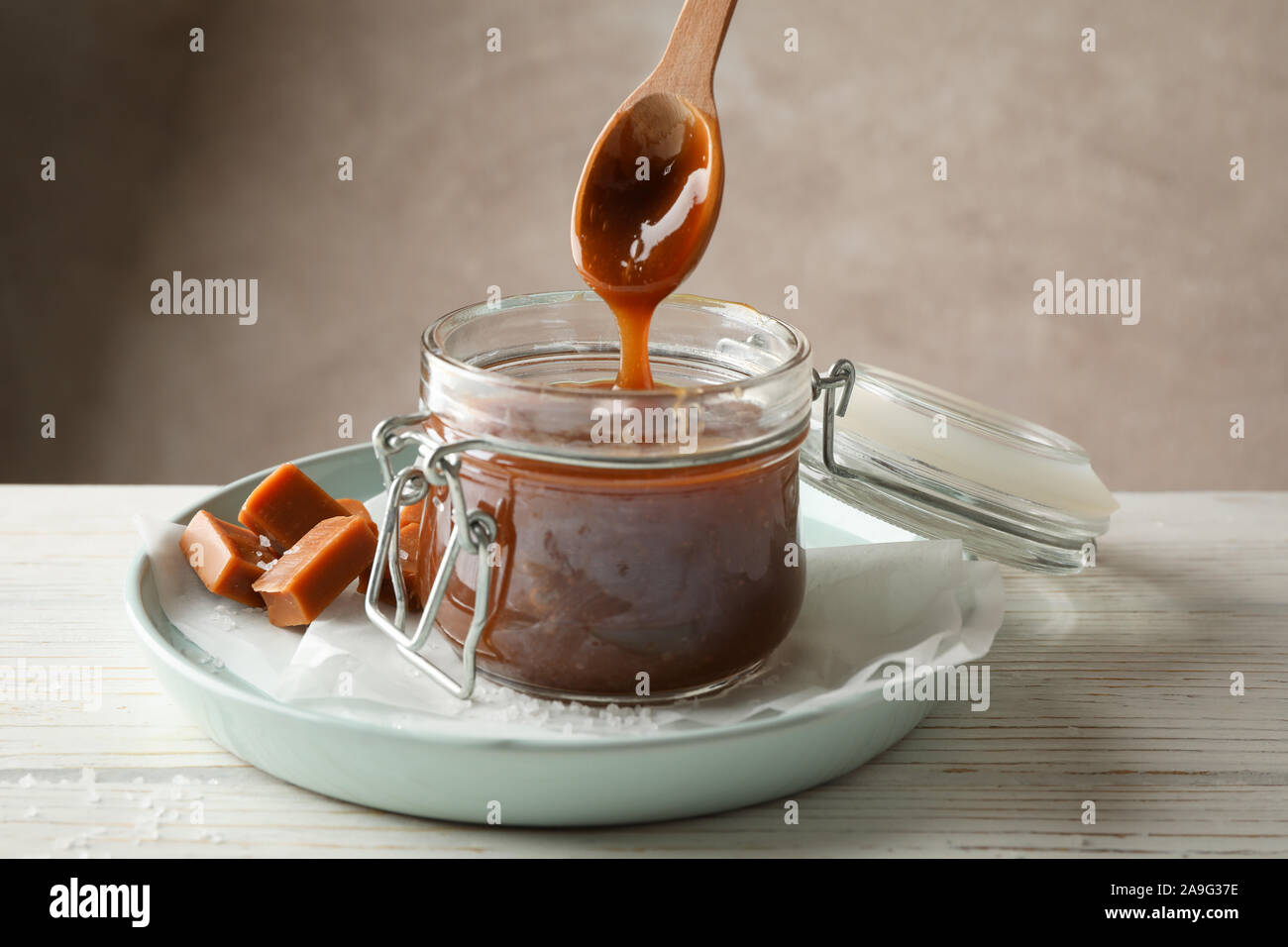 Vaso di vetro con caramello salato e caramelle su sfondo di legno, lo spazio per il testo Foto Stock