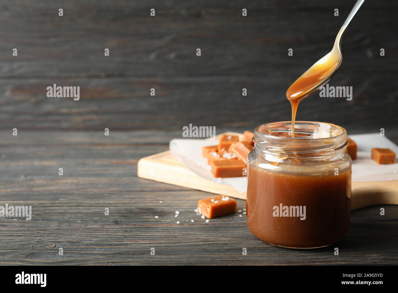 Vaso di vetro con caramello salato e caramelle su sfondo di legno, lo spazio per il testo Foto Stock