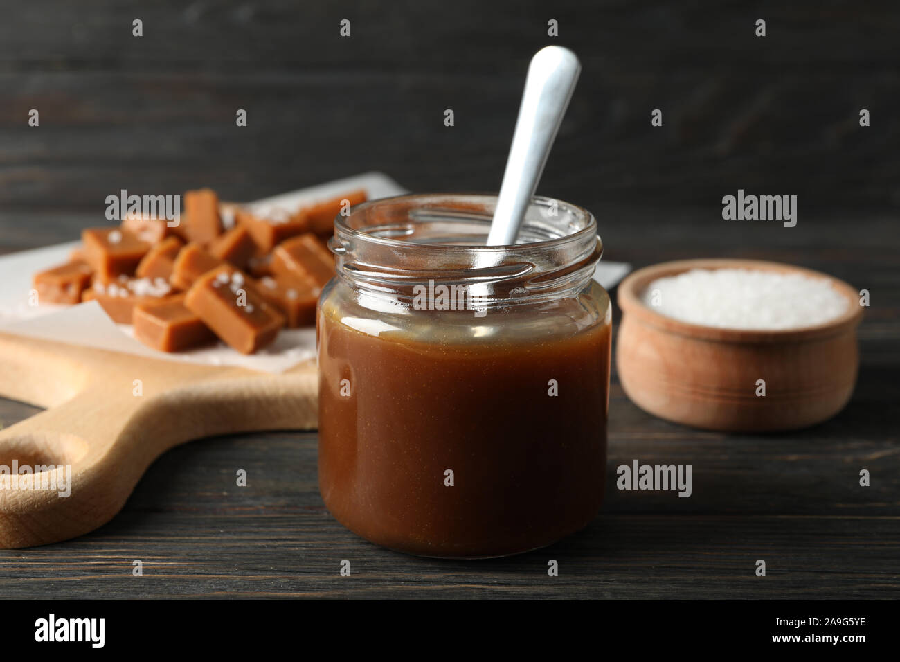 Vaso di vetro con caramello salato e caramelle su sfondo di legno, lo spazio per il testo Foto Stock