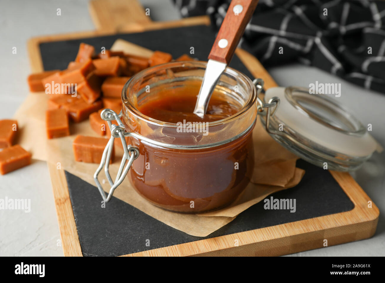 Vaso di vetro con caramello salato e caramelle su sfondo grigio, spazio per il testo Foto Stock