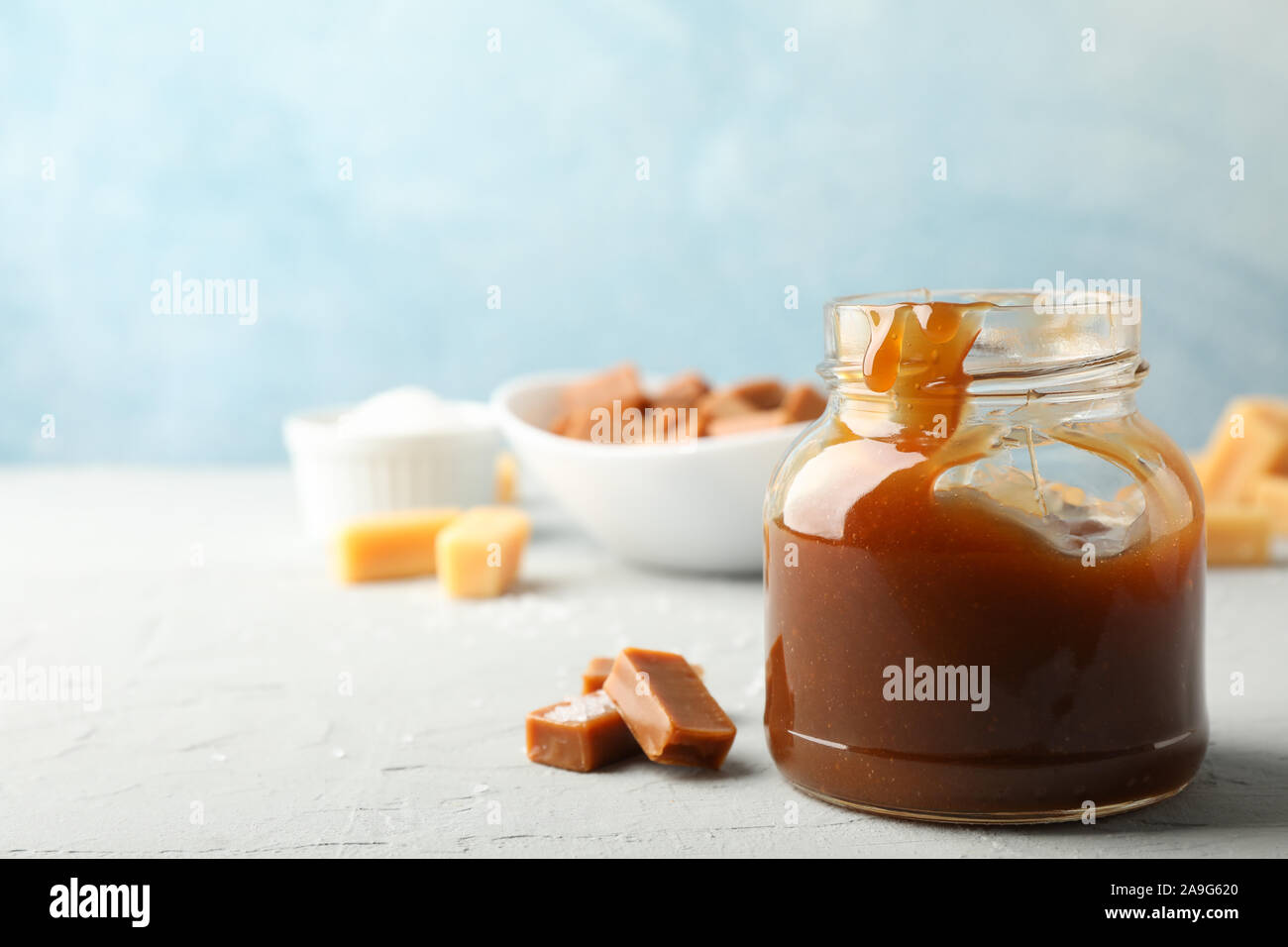 Vaso di vetro con caramello salato e caramelle su sfondo grigio, spazio per il testo Foto Stock