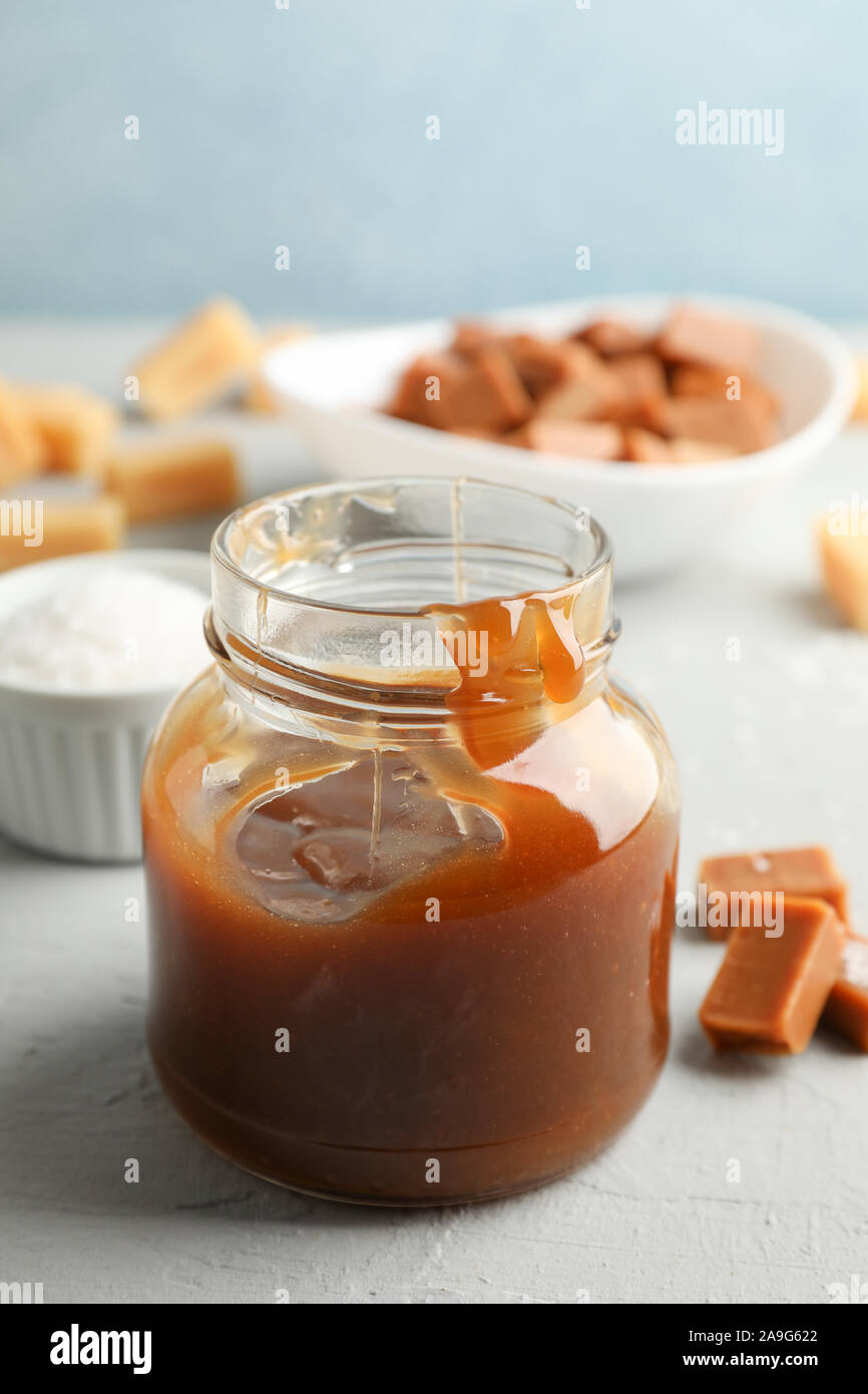 Vaso di vetro con caramello salato e caramelle su sfondo grigio, spazio per il testo Foto Stock