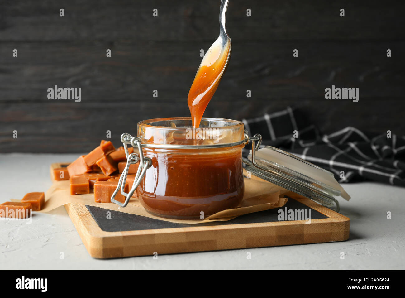 Vaso di vetro con caramello salato e caramelle su sfondo grigio, spazio per il testo Foto Stock