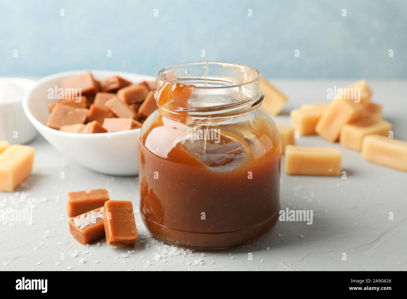 Vaso di vetro con caramello salato e caramelle su sfondo grigio, spazio per il testo Foto Stock