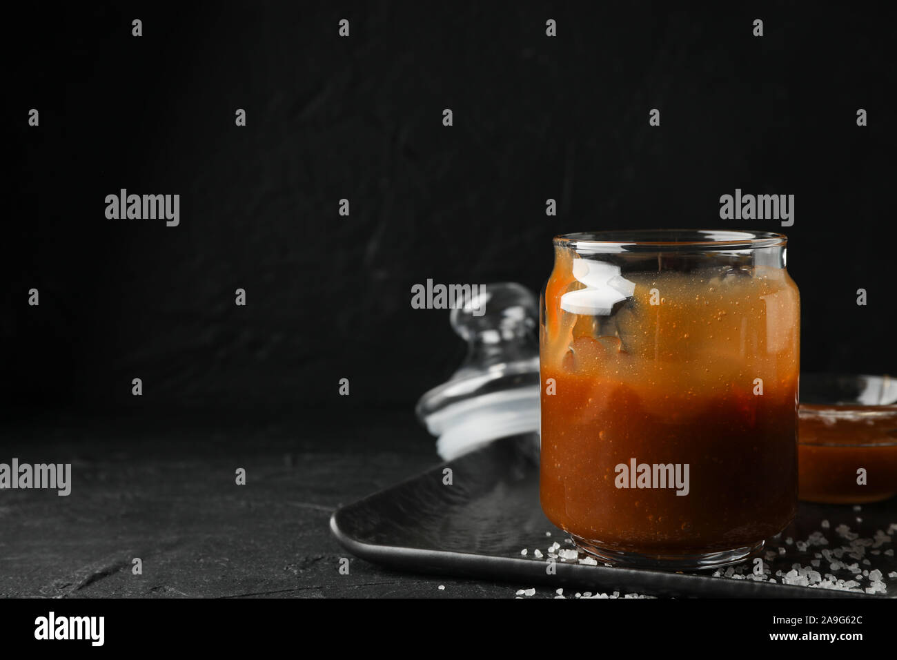 Vasi di vetro con caramello salato su sfondo nero, spazio per il testo Foto Stock
