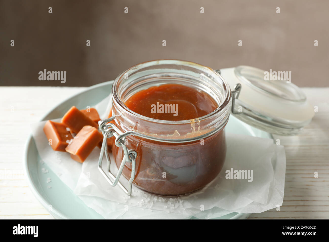 Vaso di vetro con caramello salato e caramelle su sfondo di legno, lo spazio per il testo Foto Stock