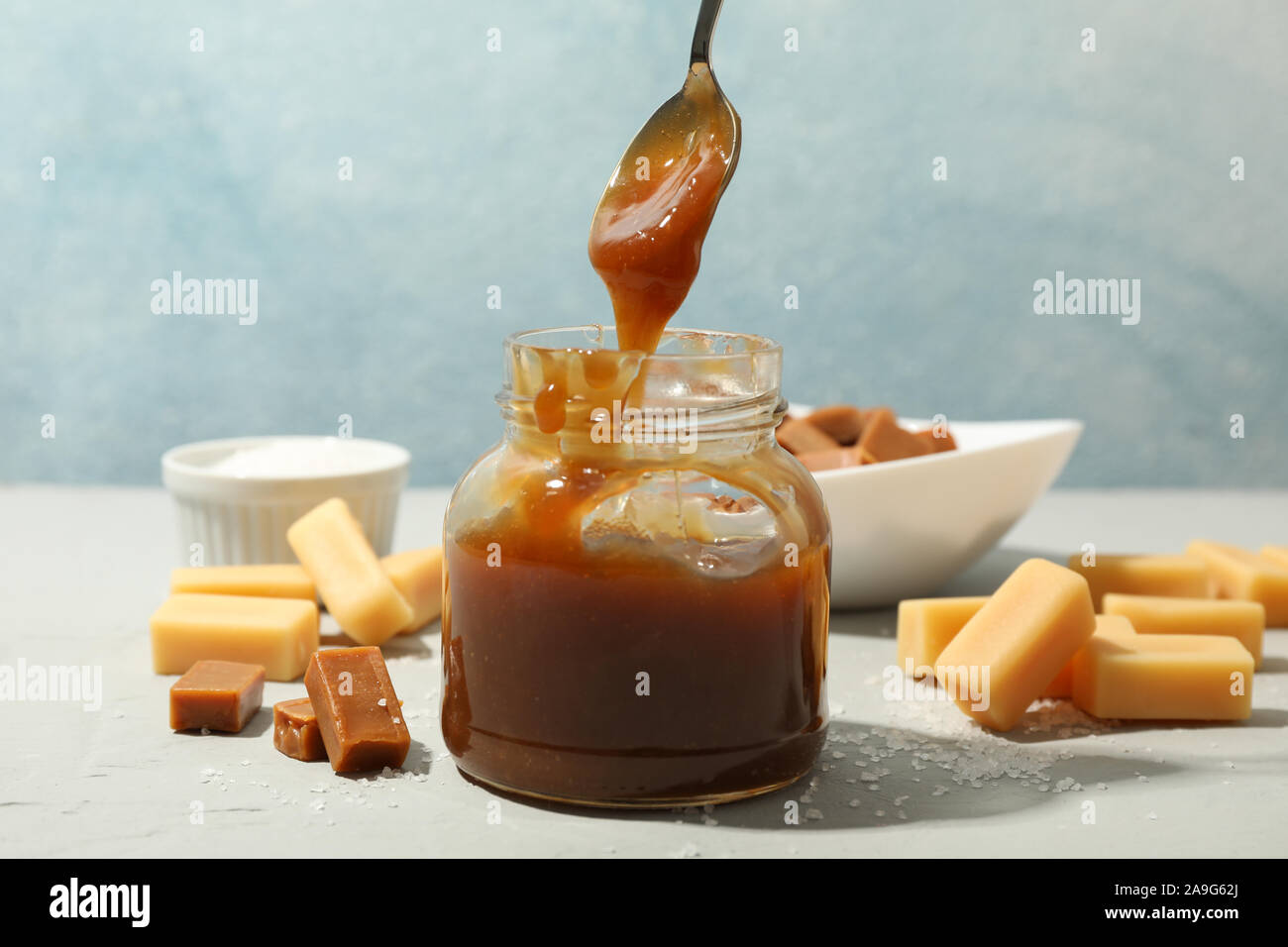 Vaso di vetro con caramello salato e caramelle su sfondo grigio, spazio per il testo Foto Stock