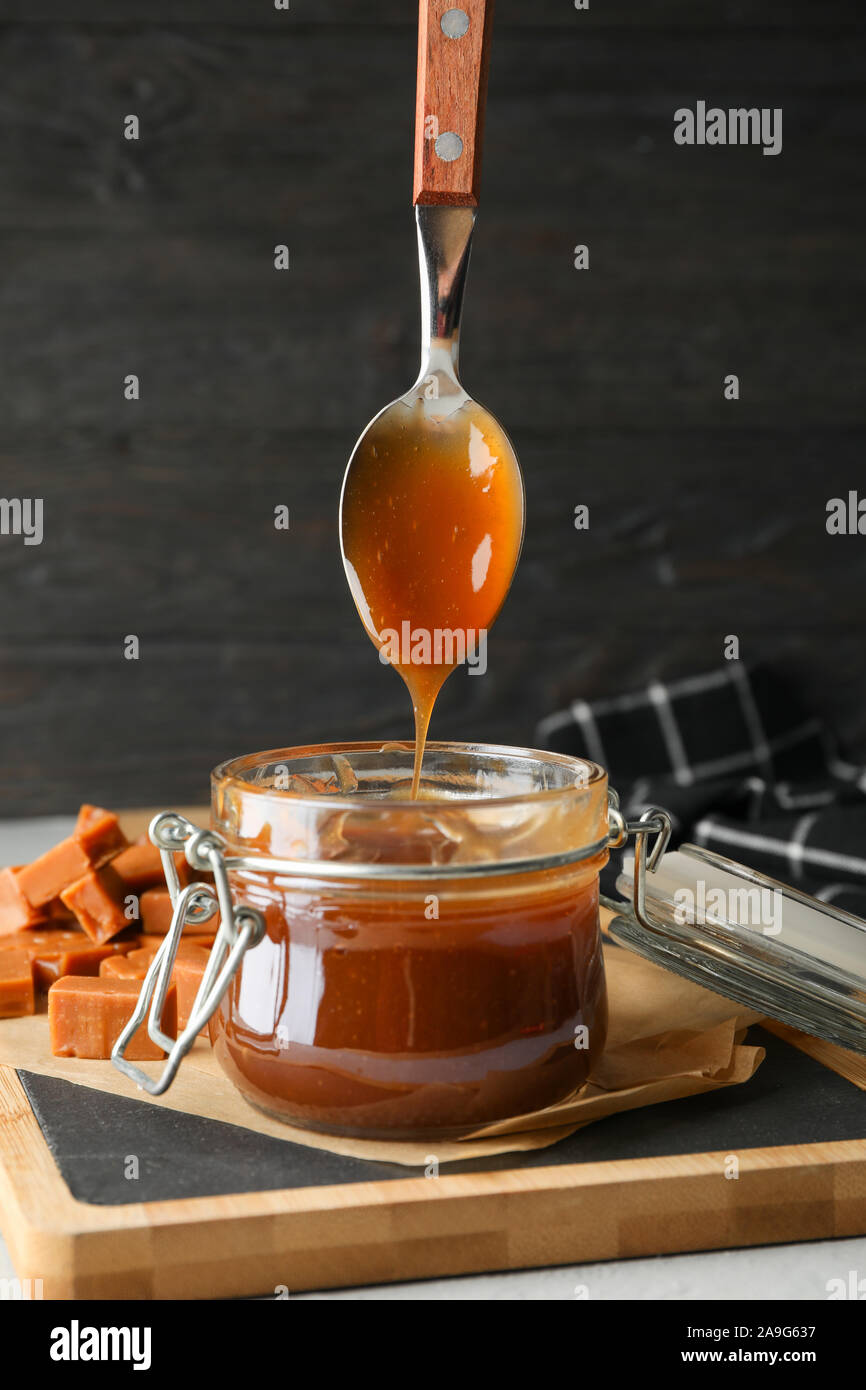 Vaso di vetro con caramello salato e caramelle su sfondo grigio, spazio per il testo Foto Stock