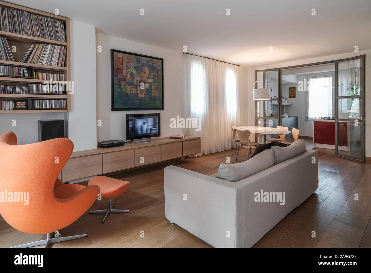 Immagine interna di un moderno soggiorno in primo piano la poltrona e il divano in tessuto di fronte alla TV in background, dopo la porta di vetro Foto Stock