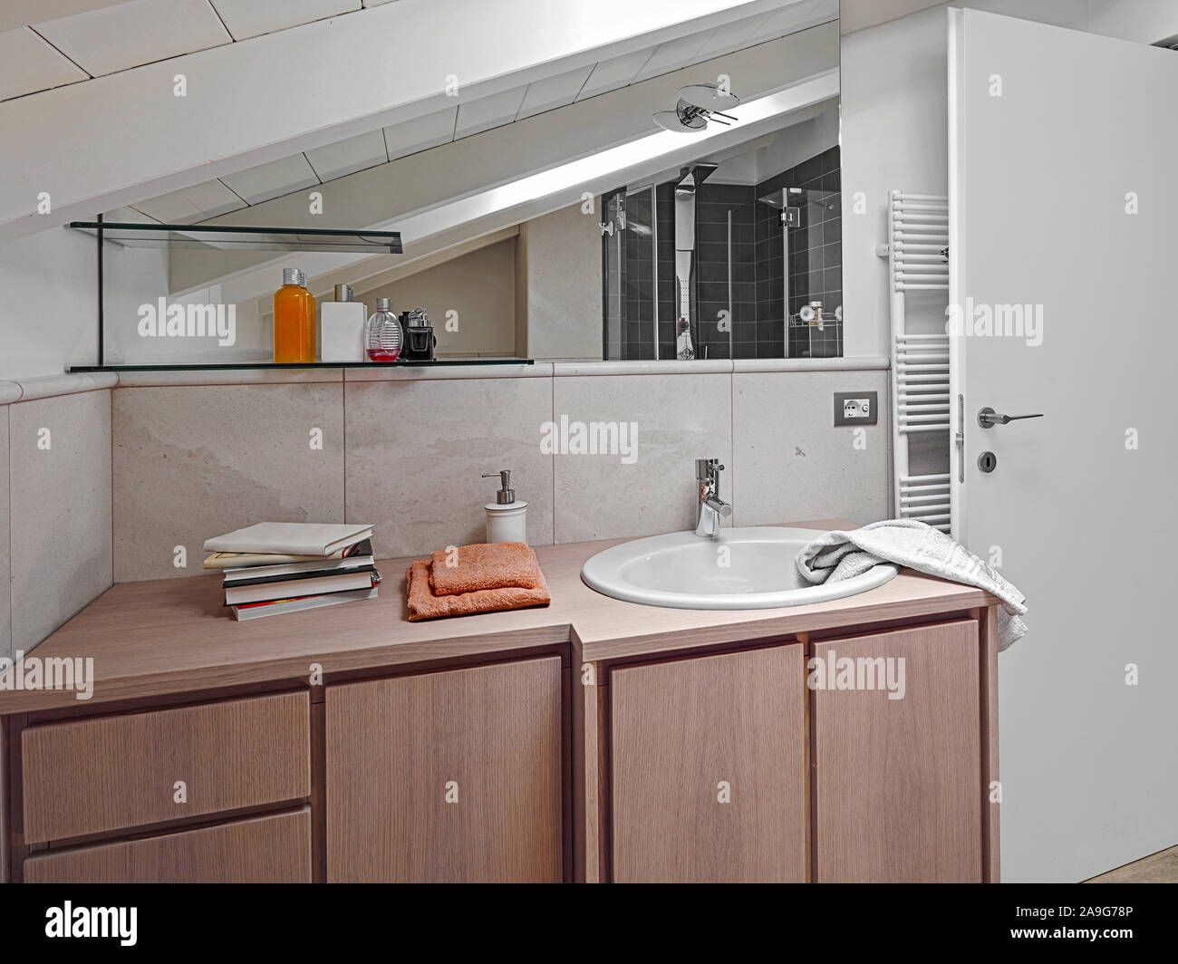 Interior shot o un bagno moderno, in primo piano la furnitre in legno con incorporato un lavandino e uno specchio grande in camera attico Foto Stock