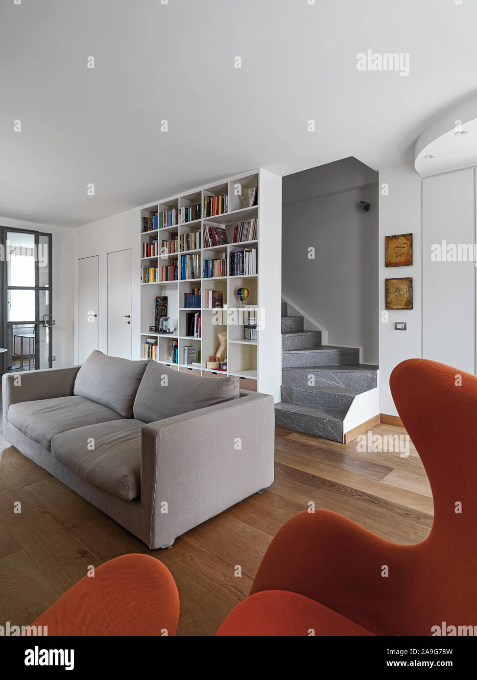 Interior shot di un moderno soggiorno in primo piano la poltrona in tessuto e tessuto divano dietro il quale vi è un bianco libreria la muratura stairca Foto Stock