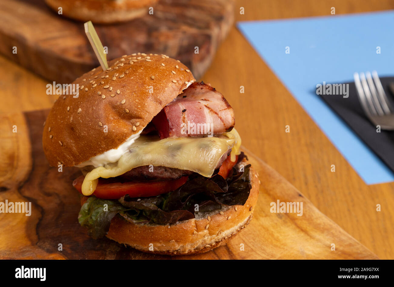 Close-up di gustosi piatti fatti in casa hamburger classico con formaggio, pancetta, lattuga, pomodoro e maionese su un tagliere di legno. Foto Stock