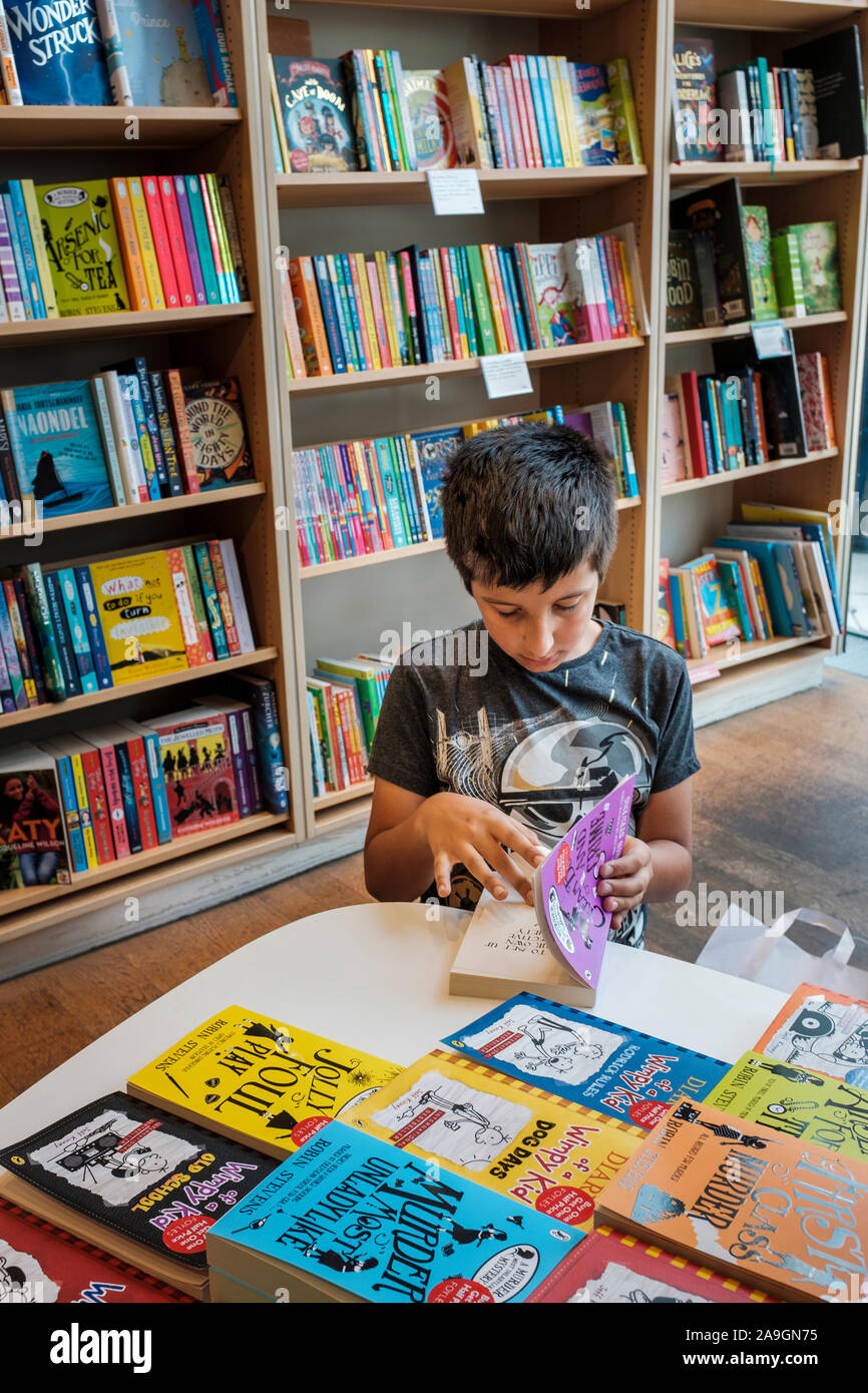 Ragazzo giovane , l'età 11, scegliendo libro nel bookshop, Londra, Inghilterra Foto Stock