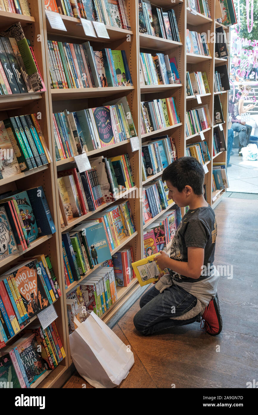 Ragazzo giovane , l'età 11, scegliendo libro nel bookshop, Londra, Inghilterra Foto Stock