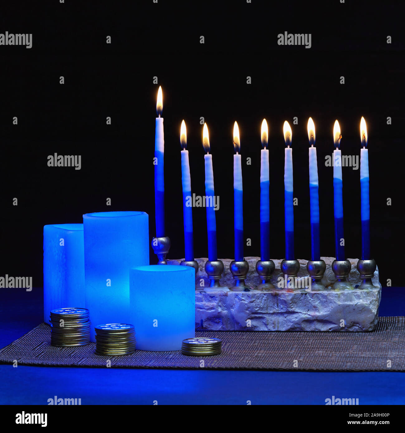 Hanukkah ancora in vita di blu brillante candele elettrica, il Menorah e pile di monete d'oro Foto Stock