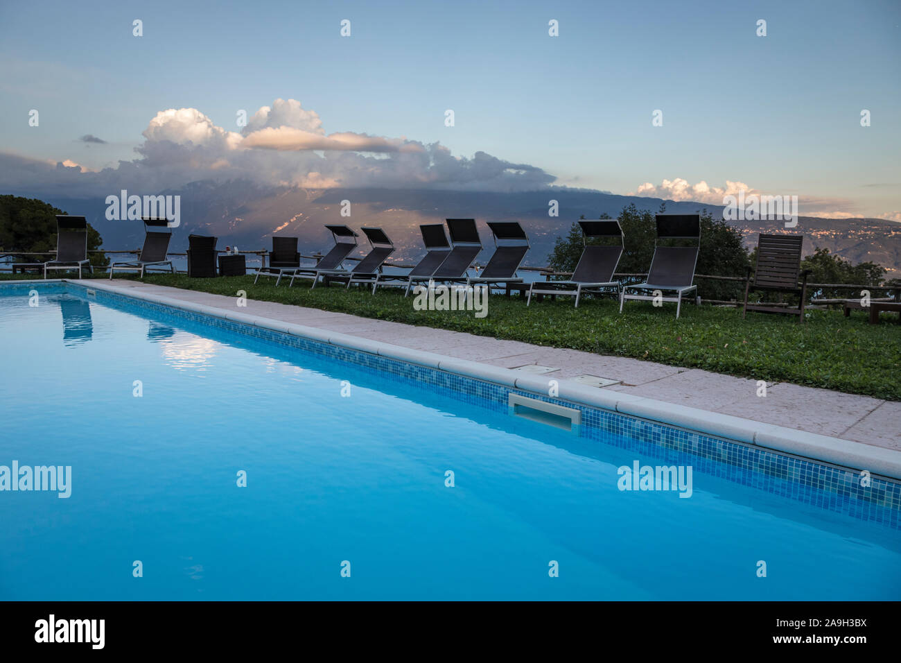 Ancora acqua blu di una piscina contornata con sedie a sdraio e un fondale sopra il lago di garda Foto Stock
