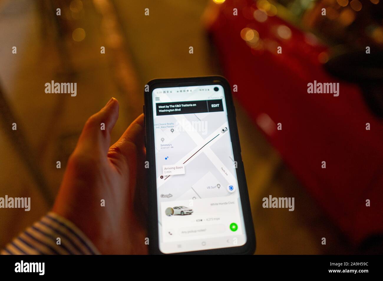 Close-up della mano di un uomo in possesso di un telefono cellulare su una strada di città di notte e utilizzando l'app Uber grandine un Uber ridesharing veicolo, Los Angeles, California, 27 ottobre 2019. Modifica nota: foto modificate per rimuovere dettagli di identificazione del driver. () Foto Stock