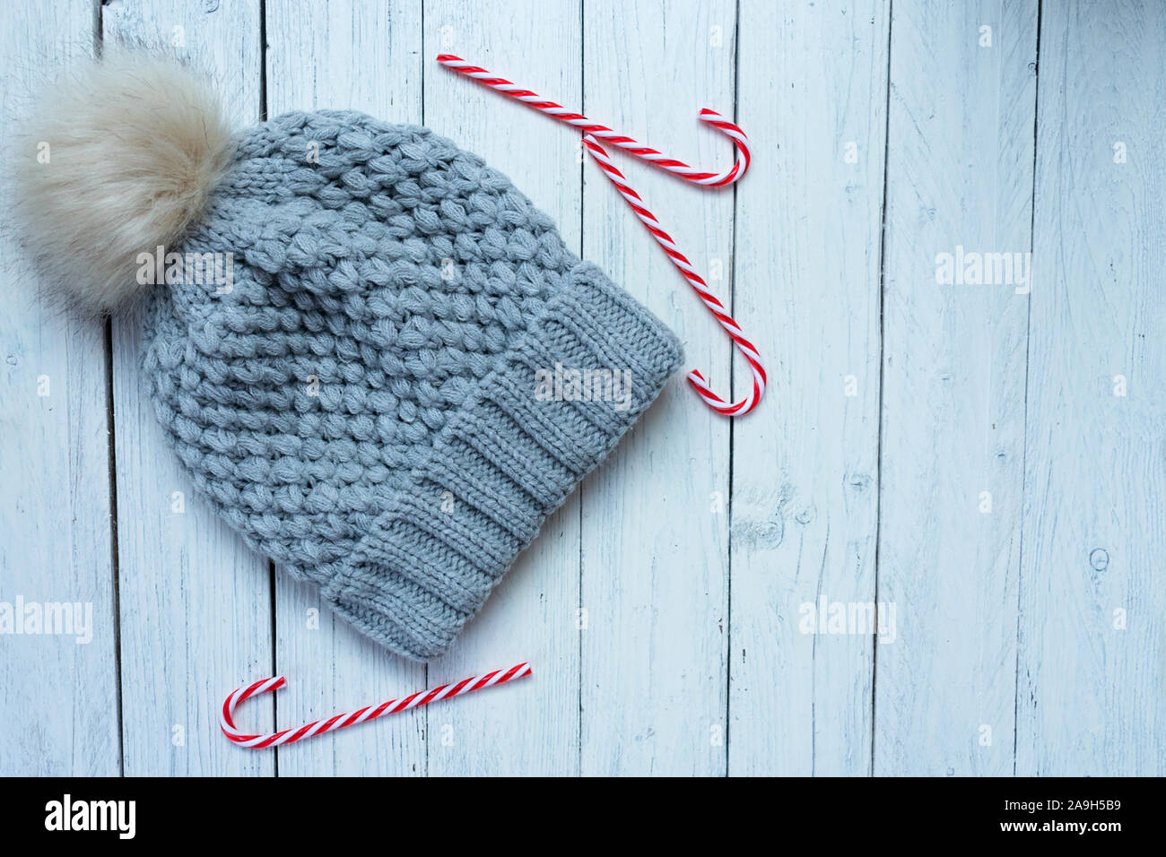 Cappello invernale e il Natale candy canes in bianco sullo sfondo di legno. Vacanze invernali concetto. Foto Stock