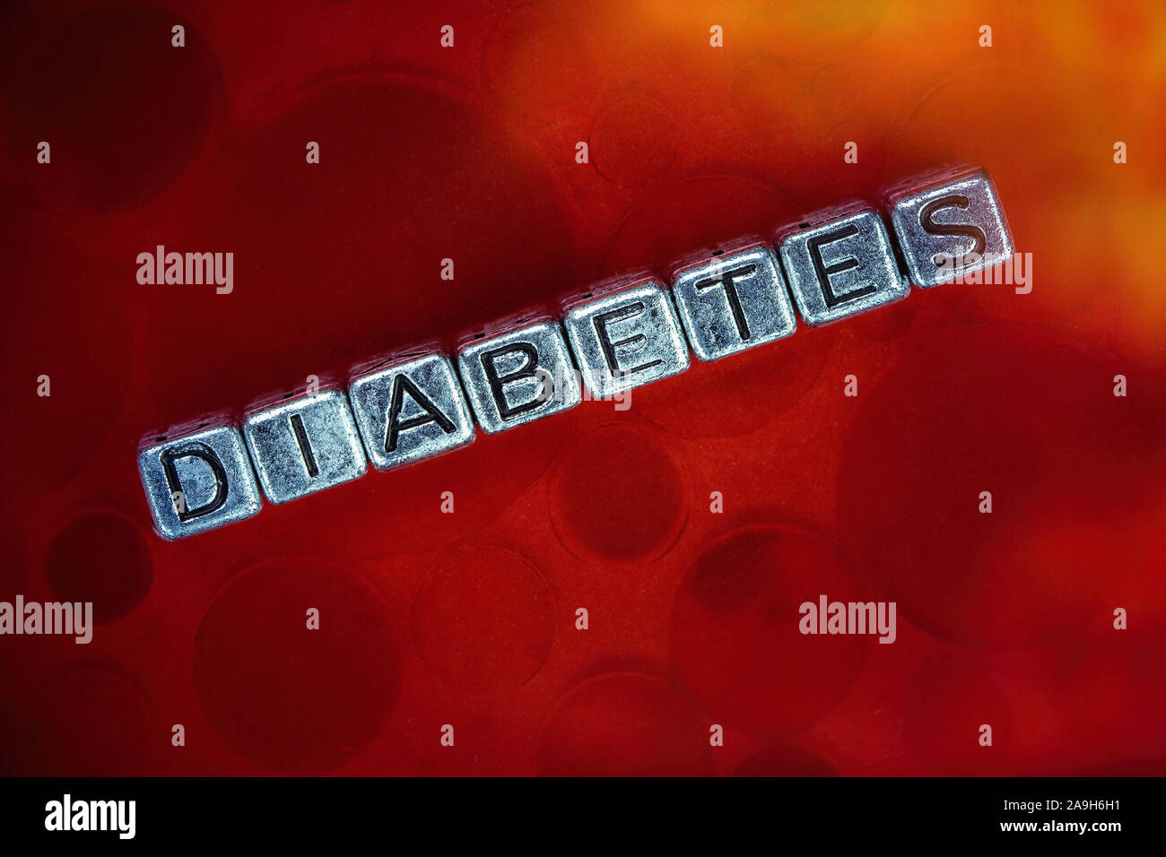 Il Diabete malattia concetto di sfondo rappresentato dal metallo cubi lettere e sfondo del sangue Foto Stock