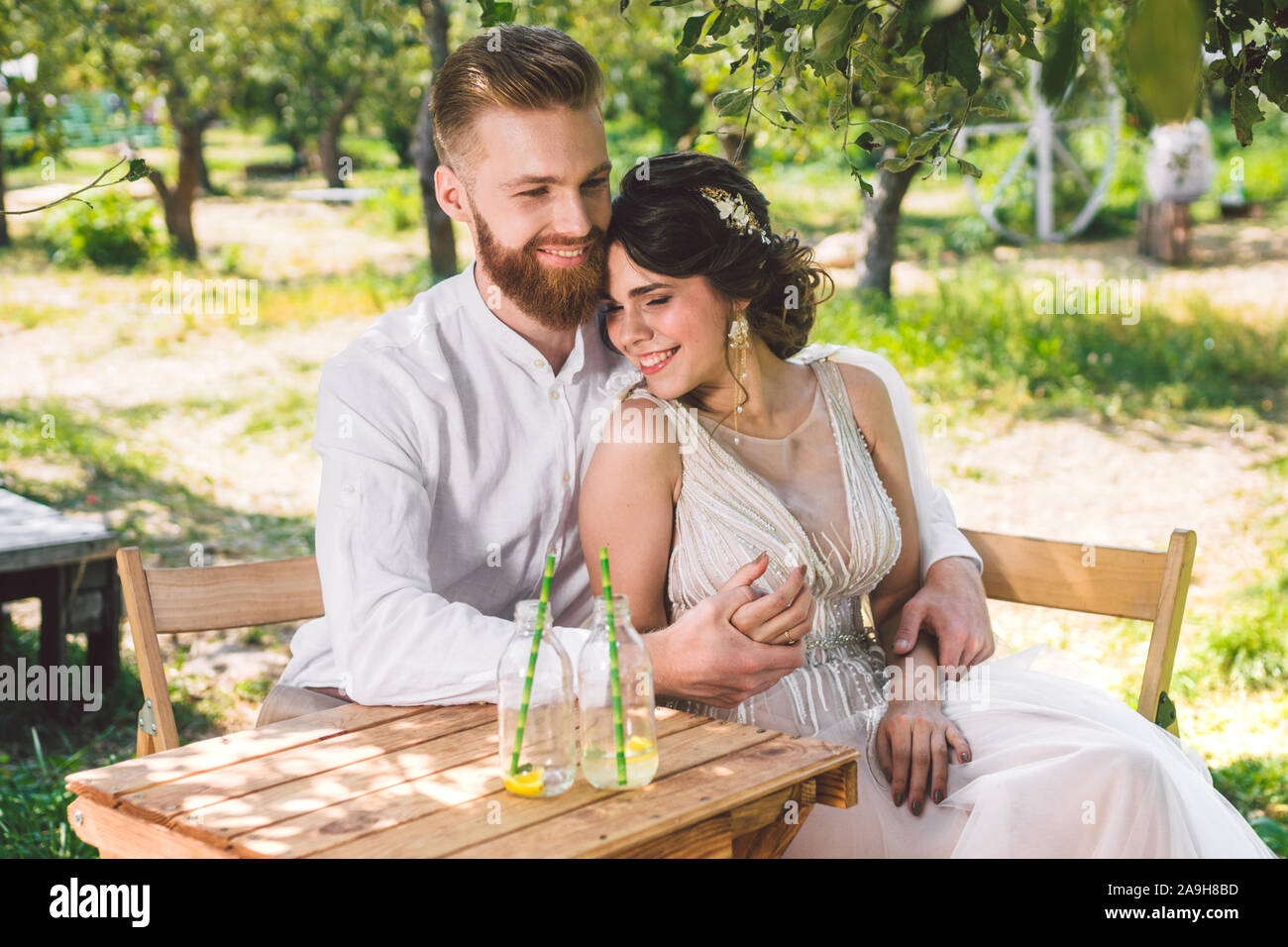 Coppia attraente sposi novelli, felice e gioioso momento. sposa e lo sposo sedersi a tavola insieme per due nel bosco. Concetto romantico data. Coppie in viaggio di nozze seduta Foto Stock
