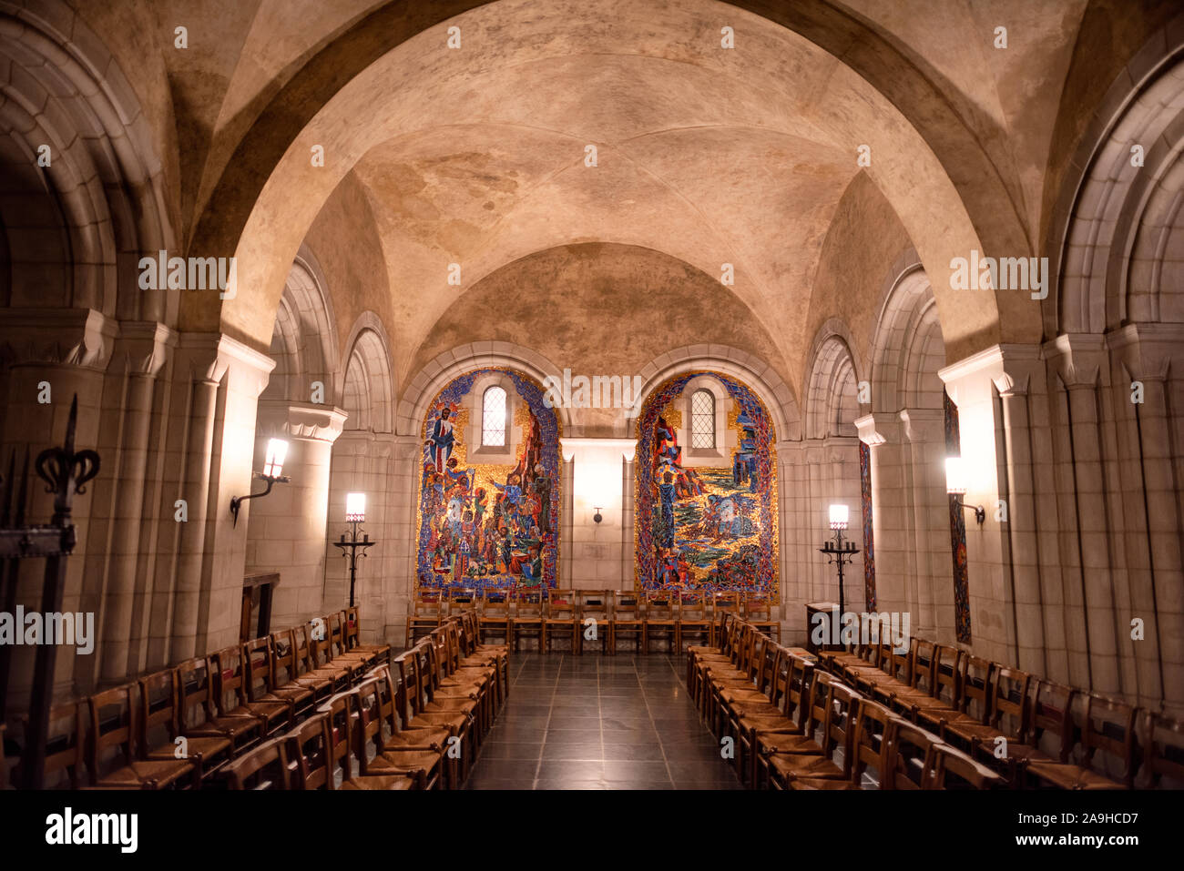 Cappella della Resurrezione nella Cattedrale Nazionale di Washington | WASHINGTON — File di sedie di legno con sedili di giunchi si affacciano su due pannelli mosaici su fondo dorato nella Cappella della Resurrezione, nella cripta della Cattedrale Nazionale di Washington a Washington, D.C. I mosaici fiancheggiano una finestra stretta sotto una volta in stile romanico, un livello di cripta costruito in uno stile ad arco arrotondato distinto dalla cattedrale gotica che si erge al di sopra. La cappella è stata aperta all'inizio degli ottantatré anni di costruzione della cattedrale, iniziata nel 1907. Foto Stock