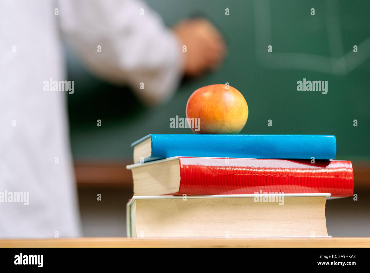 Vista ingrandita di un insegnante scrivania con una pila di libri e una mela rossa nella parte anteriore di una lavagna . Foto Stock