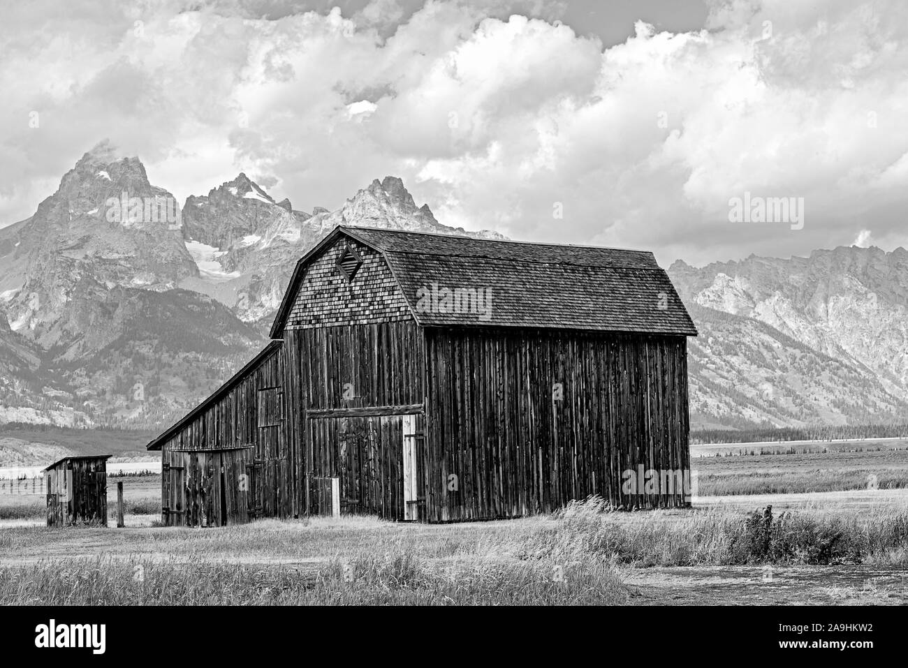 Bianco e nero, bar pionieristico e outhouse in campo con Montagne Rocciose oltre sotto cieli nuvoloso. Foto Stock